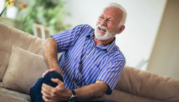 Man sitting on his couch at home, gripping his knee in pain