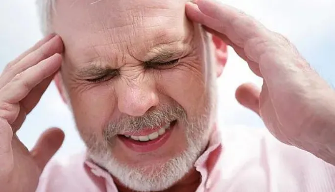 Man wincing in pain with both hands pressed to his temples