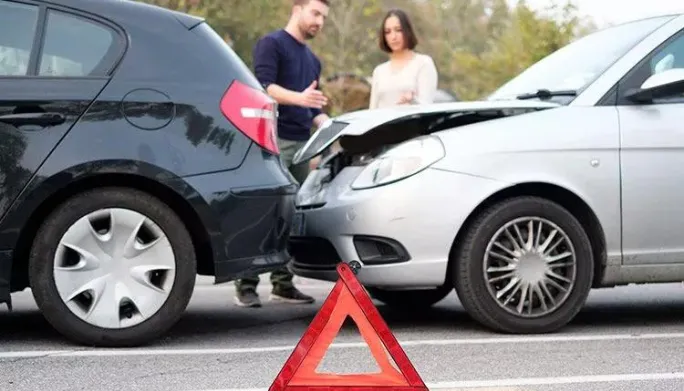 Two people standing beside a car accident with a road warning triangle