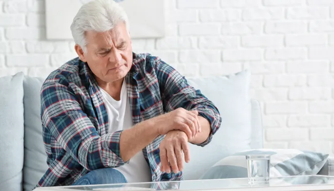 Older man at home looking down at his hand and arm