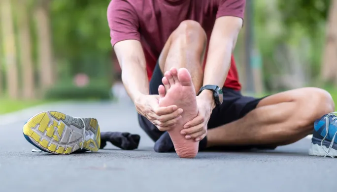 Runner sitting outdoors holding his bare foot in pain