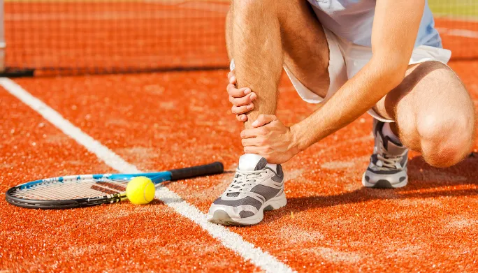 Tennis player kneeling on the court, holding his ankle in pain