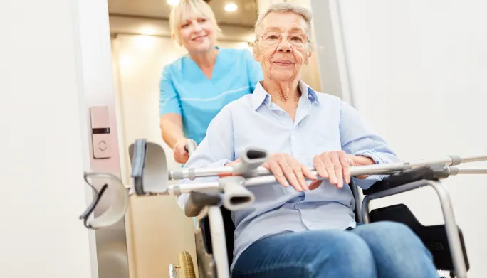 Caregiver pushing a patient in a wheelchair, crutches in hand